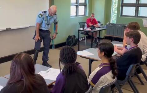 Senior Constable Jonathon Wright showing his prosthetic leg to school children. Picture from video. 