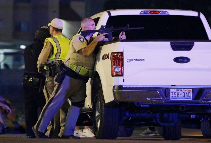 A police officer takes cover behind a truck at the scene of a shooting near the Mandalay Bay resort and casino on the Las Vegas Strip, Sunday, Oct. 1, 2017, in Las Vegas. Multiple victims were being transported to hospitals after a shooting late Sunday at a music festival on the Las Vegas Strip. (AP Photo/John Locher)