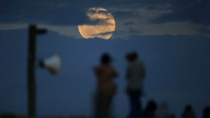 People watch as the super moon rises out of the clouds at Bondi Beach. Photo: John Veage